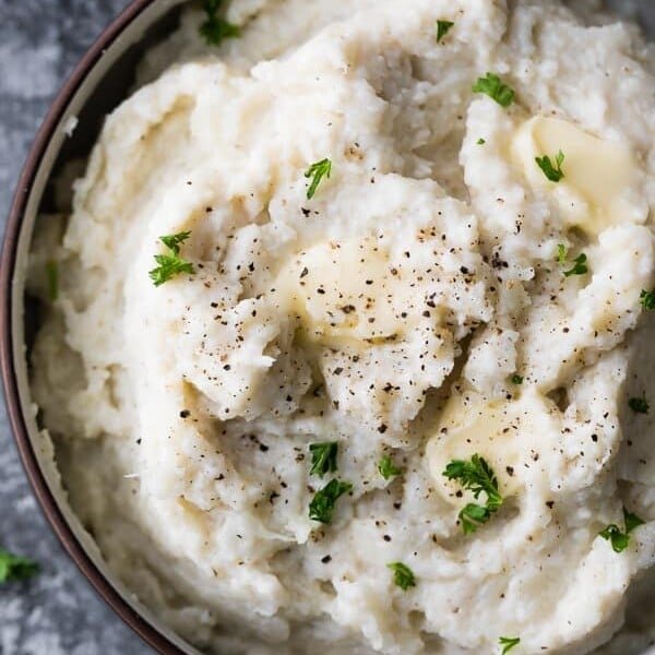 close up shot of mashed cauliflower in brown bowl with parsley