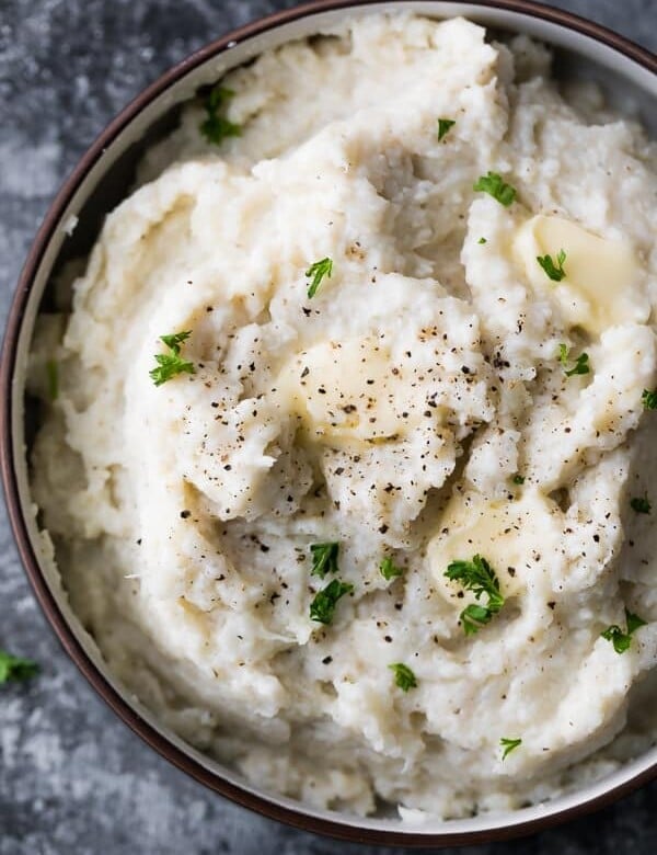 close up shot of mashed cauliflower in brown bowl with parsley