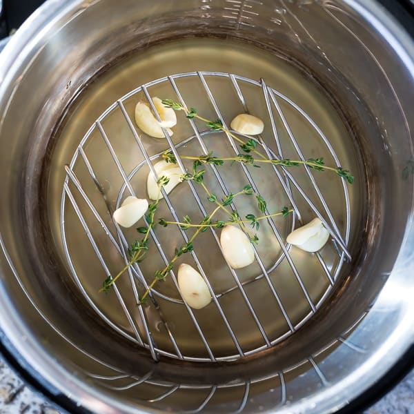 Instant Pot with stock, garlic, thyme leaves and trivet to cook cauliflower mash
