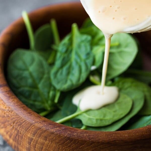 pouring maple tahini dressing onto a salad