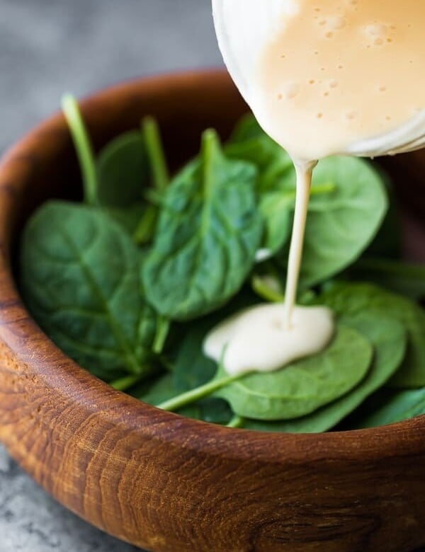 pouring maple tahini dressing onto a salad
