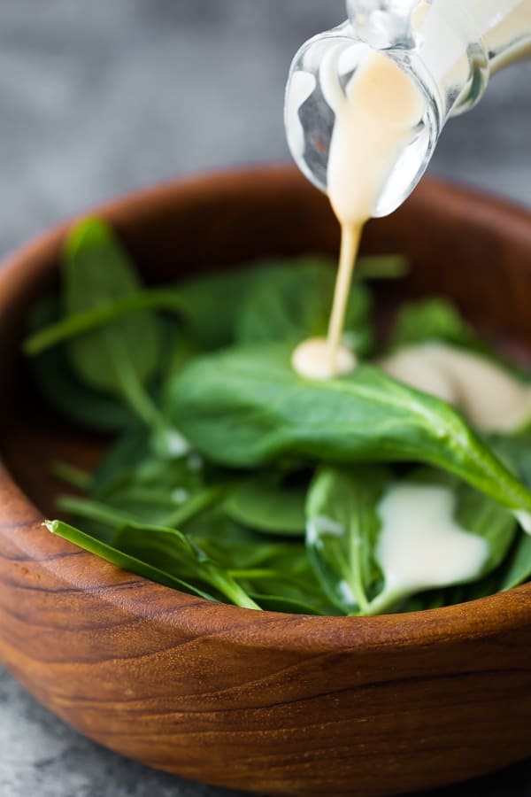 pouring tahini dressing onto greens