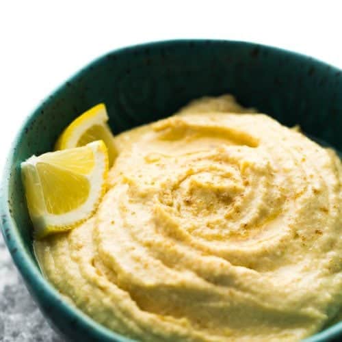 close up of a blue bowl filled with hummus and lemon slices