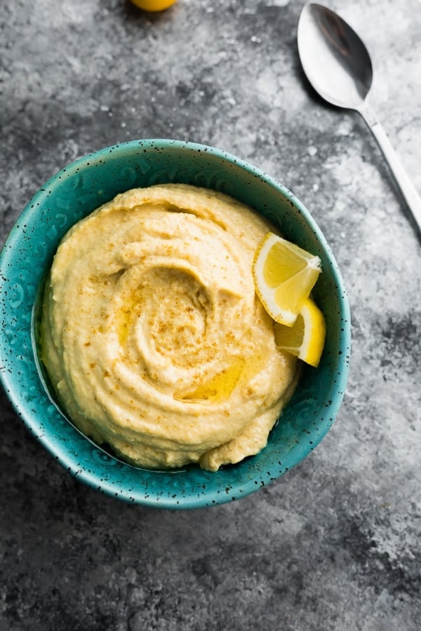 overhead shot of hummus in blue bowl with lemon wedges and spoon on counter