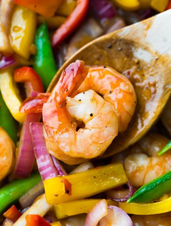 close up shot of wood spoon with two shrimp on it in sweet chili stir fry