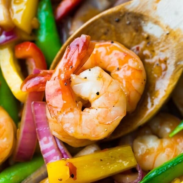 close up shot of wood spoon with two shrimp on it in sweet chili stir fry
