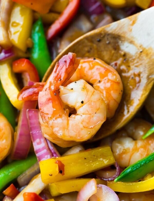 close up shot of wood spoon with two shrimp on it in sweet chili stir fry