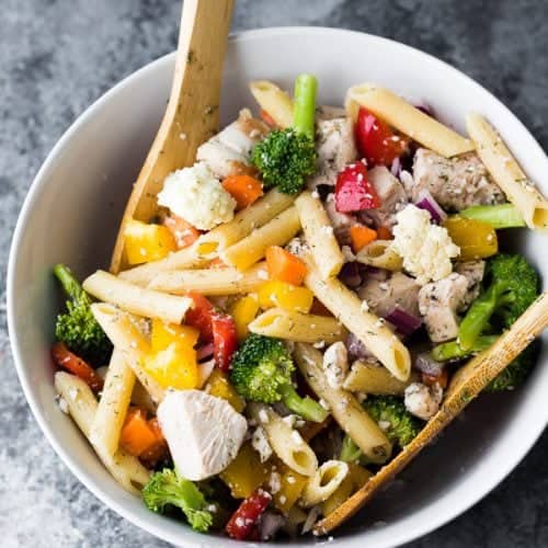 Overhead shot of healthy Greek chicken pasta salad in a white bowl with wooden spoon