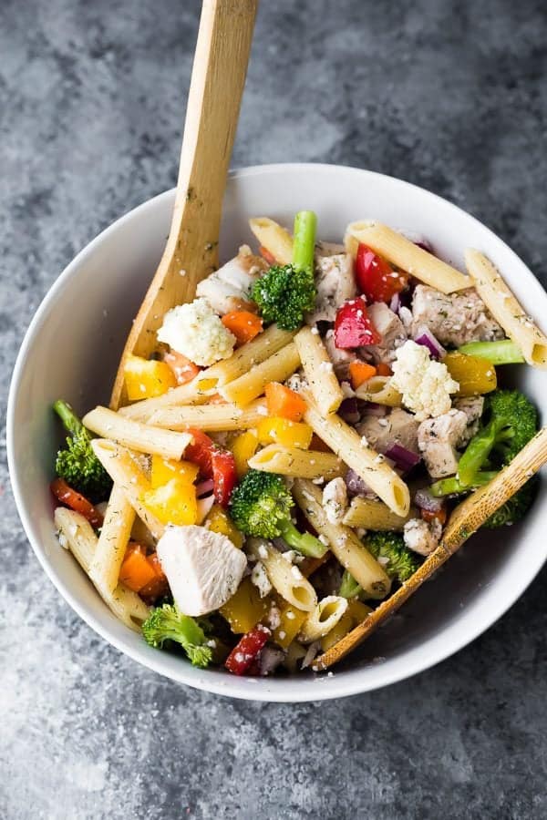 Overhead shot of healthy Greek chicken pasta salad in a white bowl with wooden spoon