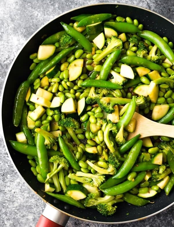 ginger teriyaki stir fry with broccoli snap peas and greens in skillet with wood spoon