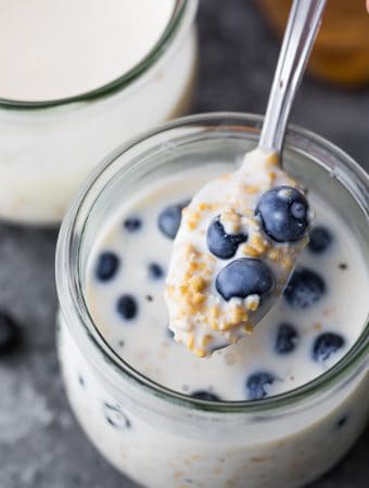 spoon taking out a scoop of overnight steel cut oats in mason jar with fresh blueberries