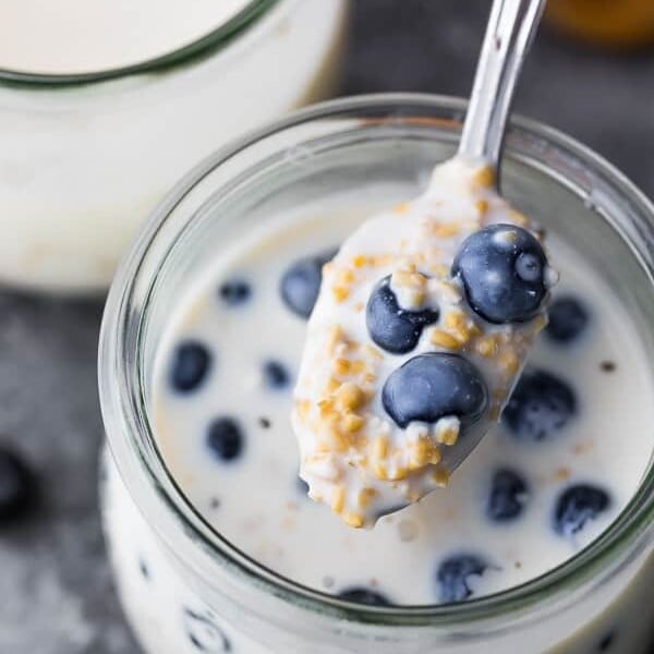 spoon taking out a scoop of overnight steel cut oats in mason jar with fresh blueberries