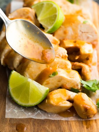 Close up shot of chipotle lime chicken breasts with a spoon drizzling sauce on top and fresh lime wedges