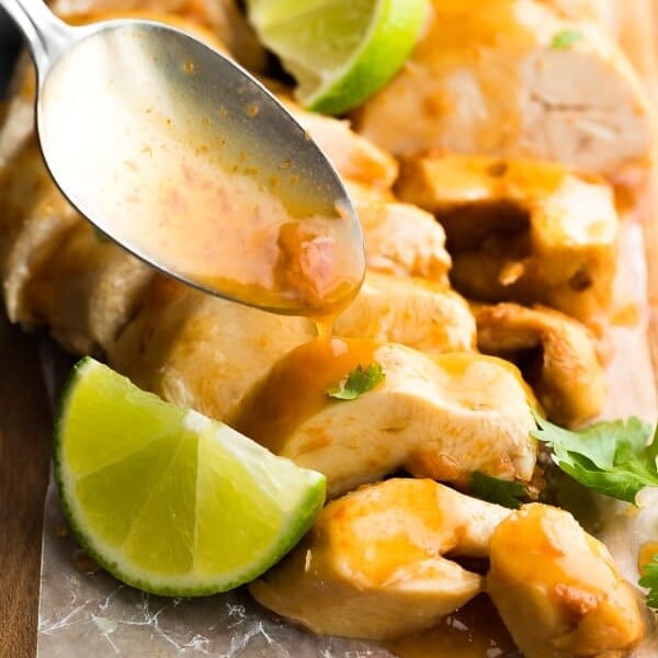 Close up shot of chipotle lime chicken breasts with a spoon drizzling sauce on top and fresh lime wedges