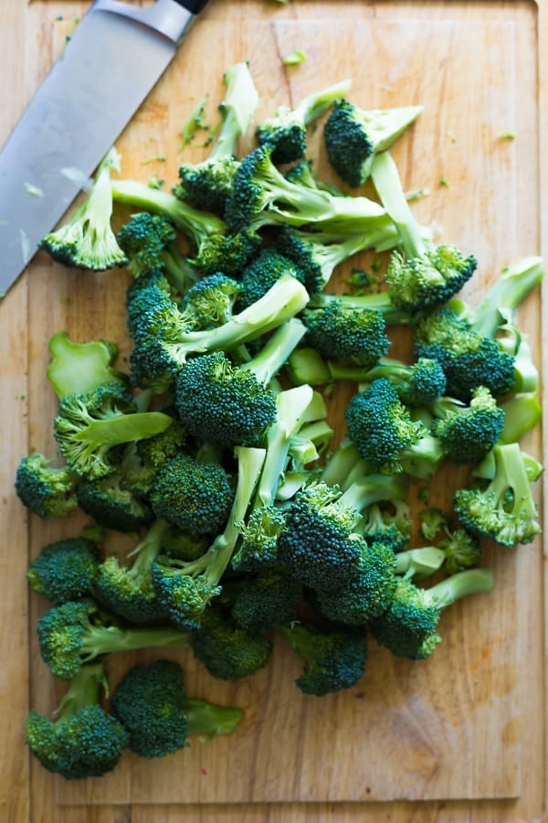 overhead shot of broccoli florets and large knife on a wood cutting board