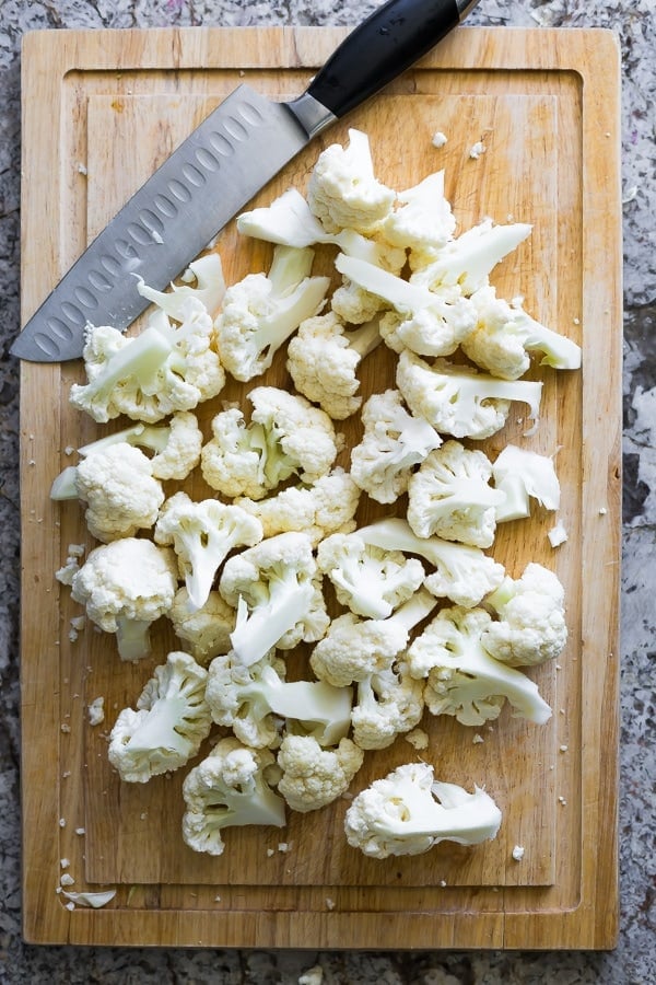 overhead view of caulfilower florets and knife on wood cutting board