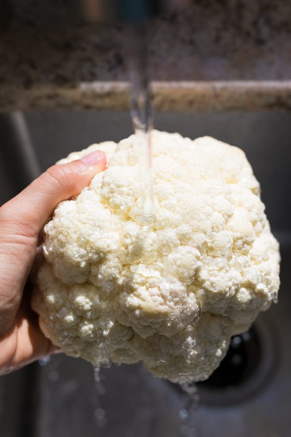 hand holding a head of cauliflower under running tap