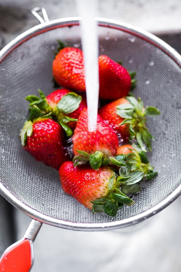 water being poured over strawberries in a sieve