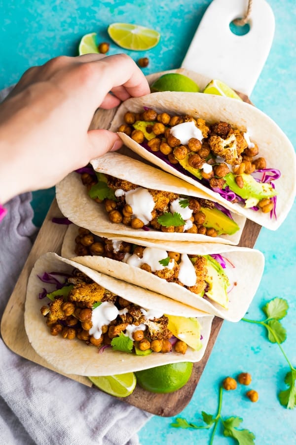 Hand grabbing a Air Fryer Cauliflower Chickpea Taco on cutting board with blue background