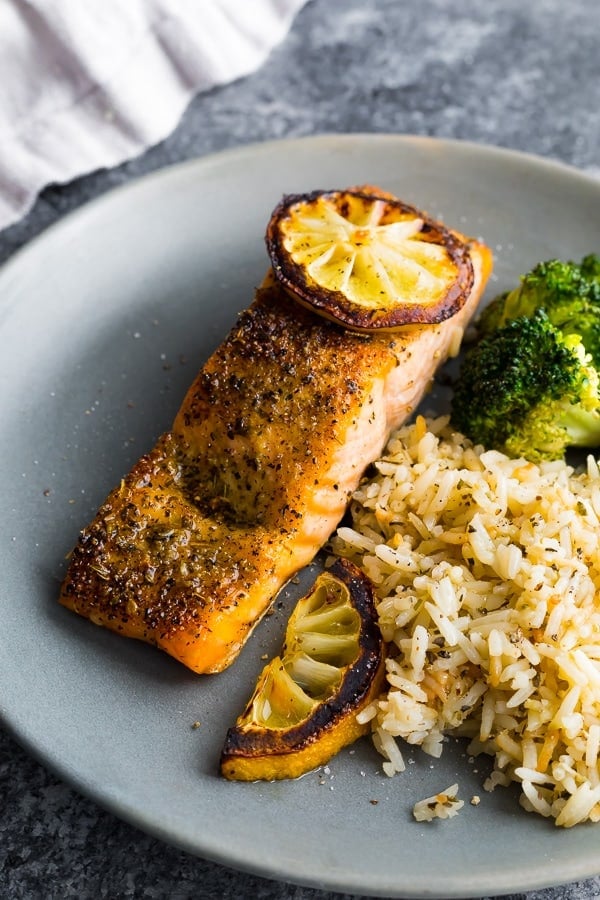 herb crusted broiled salmon on plate with rice, charred lemons and broccoli