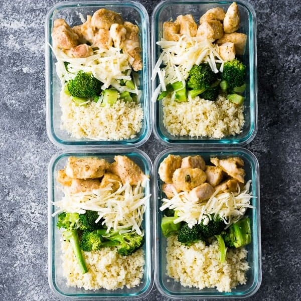 overhead shot of four glass containers with cheesy chicken rice and broccoli bowls