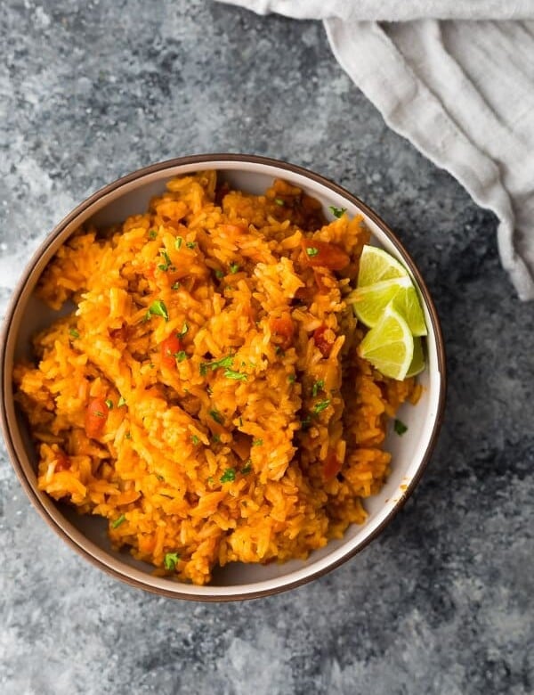overhead shot of mexican rice with lime wedges in brown bowl on gray counter