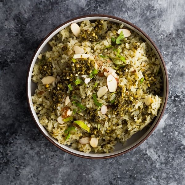 overhead shot of pesto green rice in brown bowl on gray background
