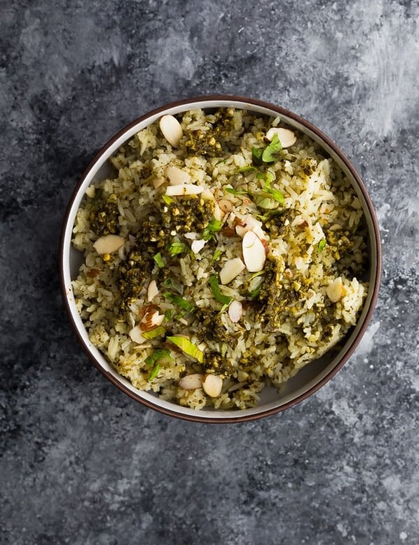 overhead shot of pesto green rice in brown bowl on gray background