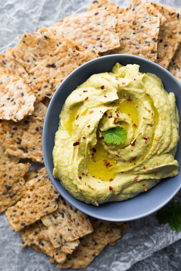 Creamy Avocado Hummus in blue bowl surrounded by crackers