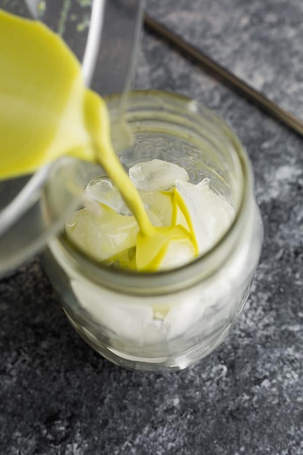 pouring a matcha latte recipe into a glass filled with ice