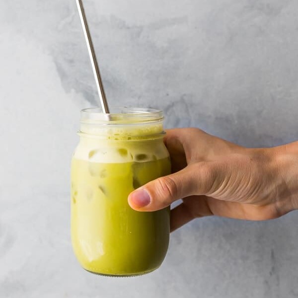 hand holding a glass mason jar with iced matcha latte and straw