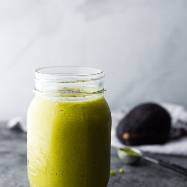 side view of matcha avocado smoothie in glass mason jar with avocado in background