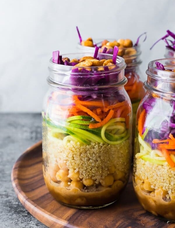 Close up shot of mason jars filled with thai chickpea mason jar salad on wood tray