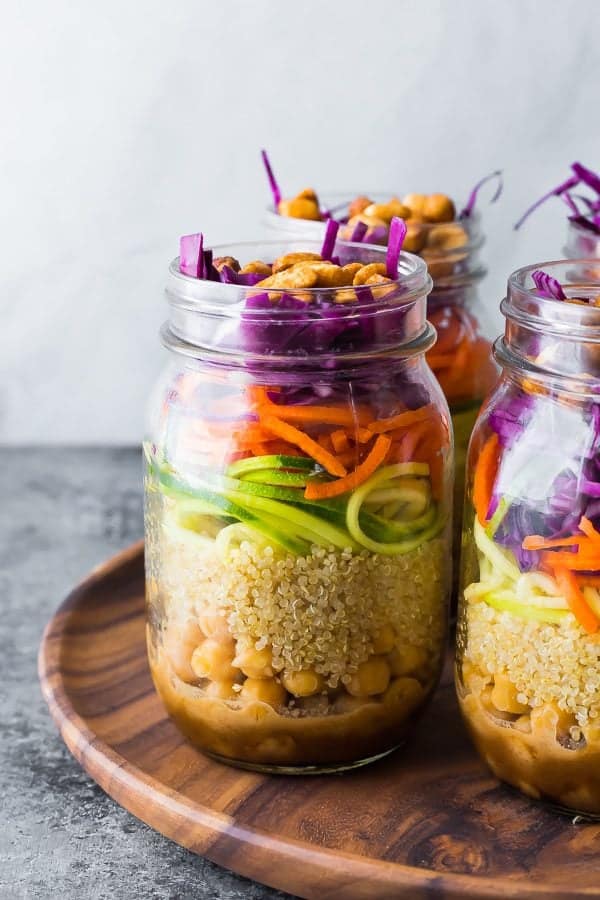 Close up shot of mason jars filled with thai chickpea mason jar salad on wood tray