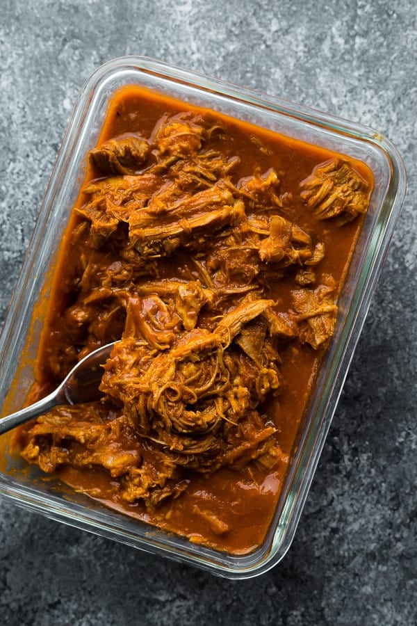 overhead shot of pulled pork in glass meal prep container with fork