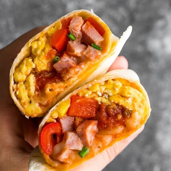 hand holding breakfast burrito cut in half