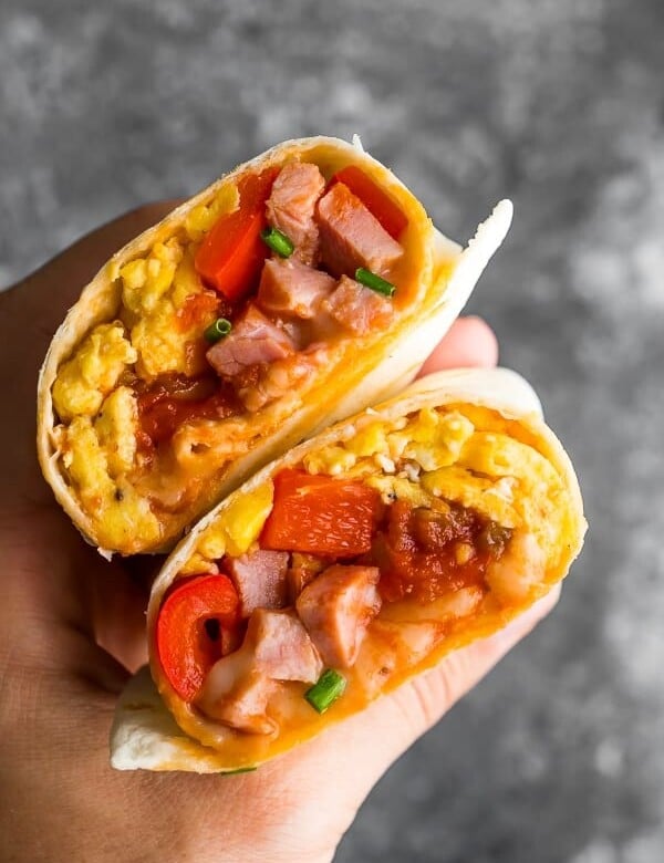 hand holding breakfast burrito cut in half