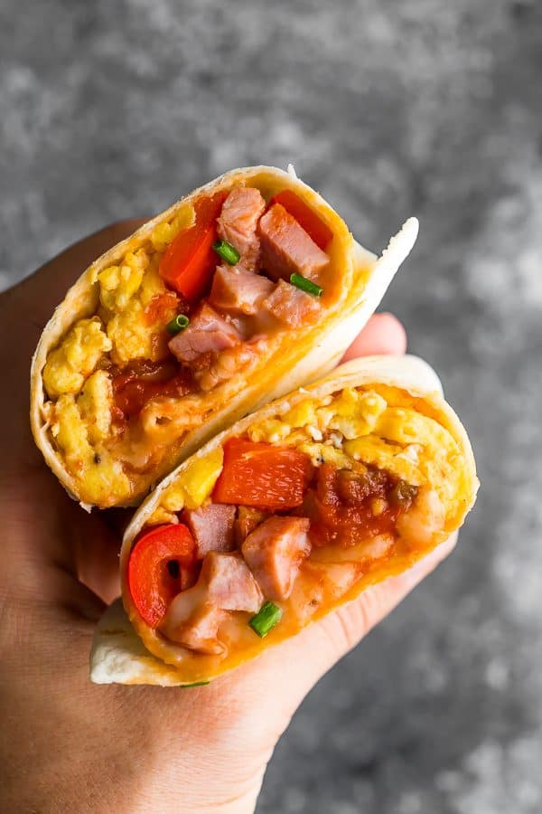 hand holding breakfast burrito cut in half