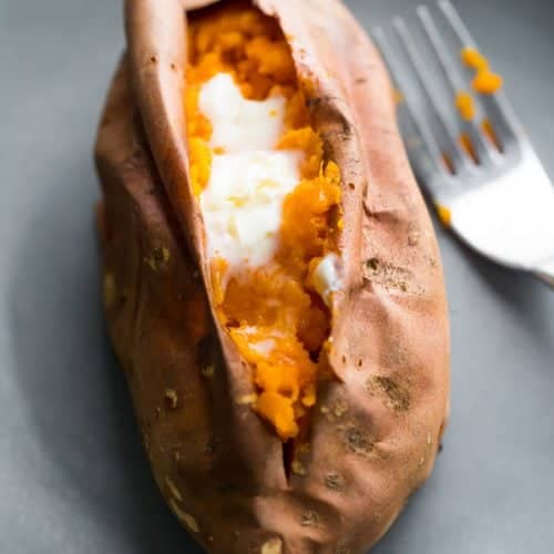 baked sweet potato with butter on gray plate with a fork
