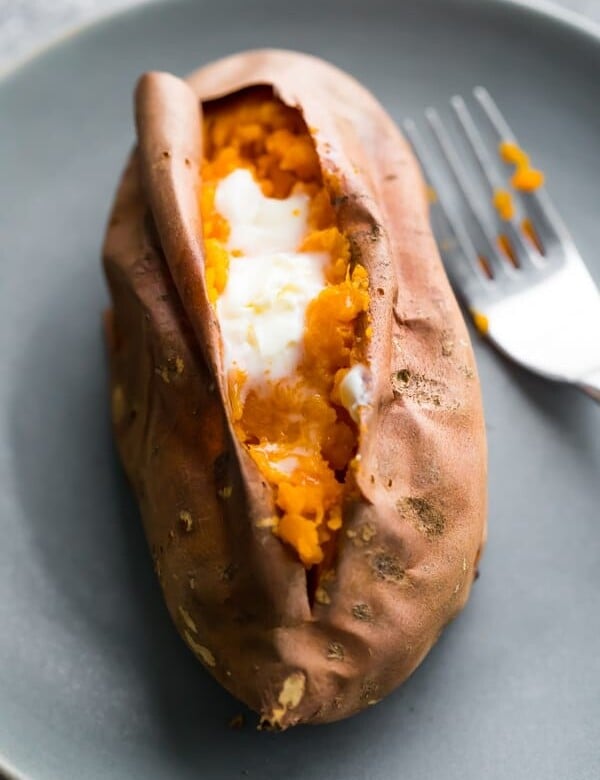 baked sweet potato with butter on gray plate with a fork