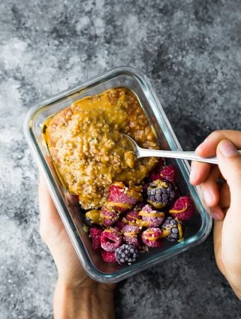 hands holding a glass meal prep container filled with instant pot steel cut oats and berries