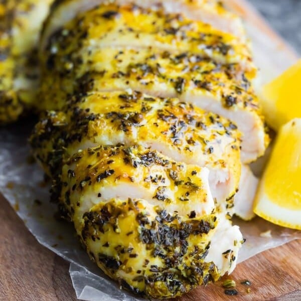 sliced lemon pepper chicken on wood cutting board with fresh lemon slices