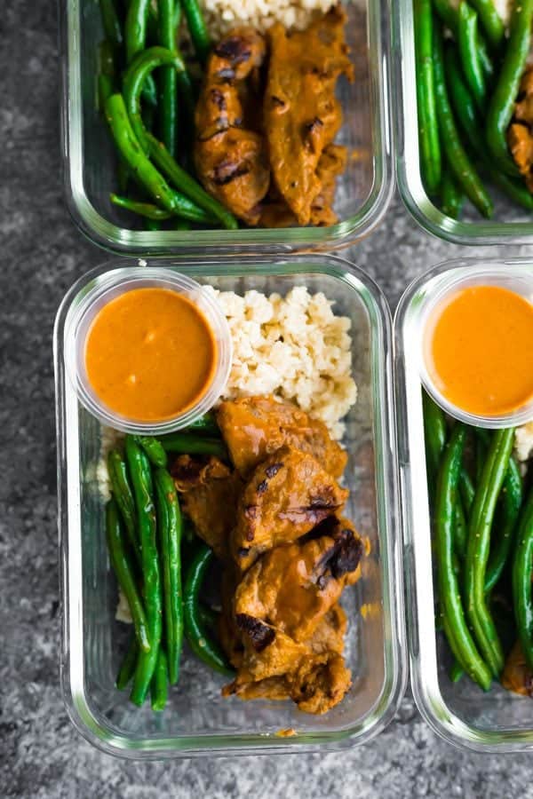 overhead shot of satay beef with green beans in four glass meal prep containers