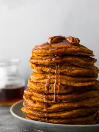 stack of pumpkin pancakes with a jar of syrup in the background