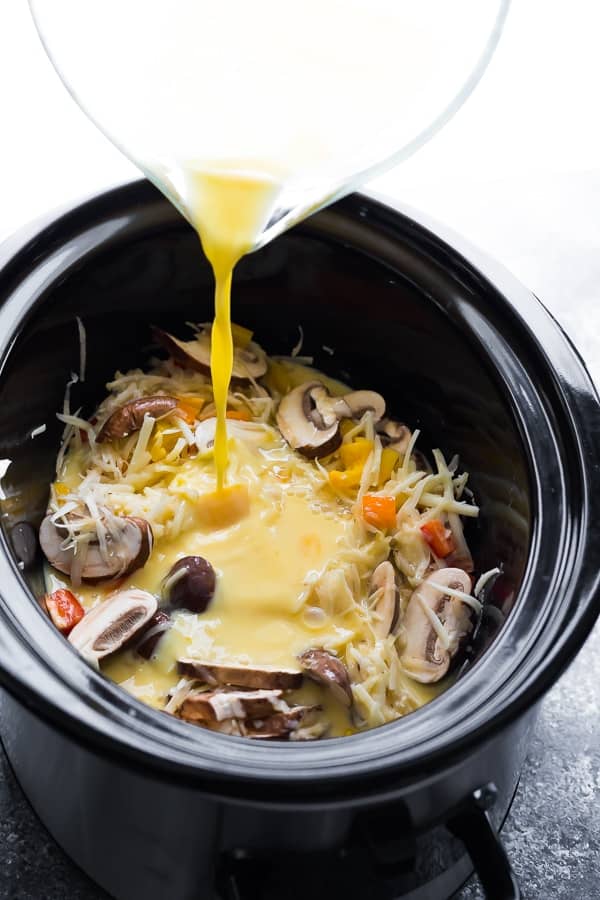 pouring the egg mixture over the crock pot breakfast casserole