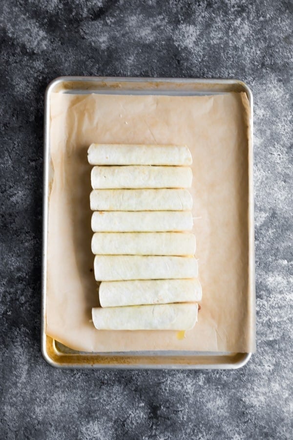 baked taquitos rolled up on baking sheet