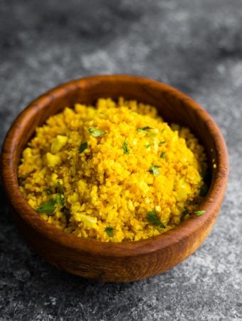 golden turmeric cauliflower rice in wood bowl on gray background