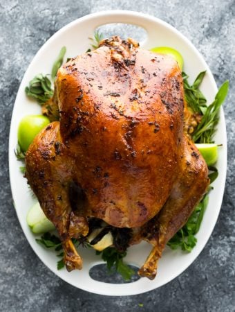 overhead shot of a cooked turkey with garlic sage butter on a white platter with fresh herbs