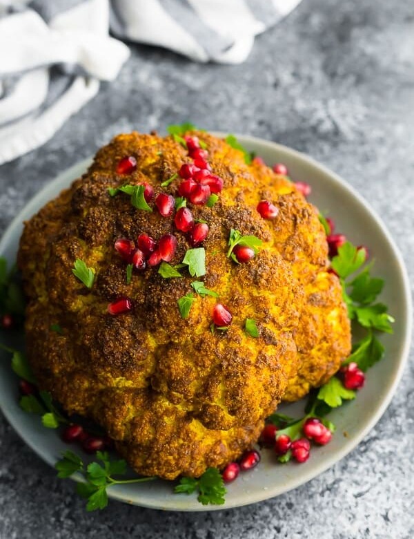 whole roasted cauliflower on gray plate with parsley and pomegranate seeds