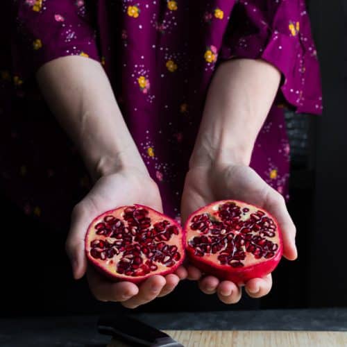 hand holding out a pomegranate cut in half